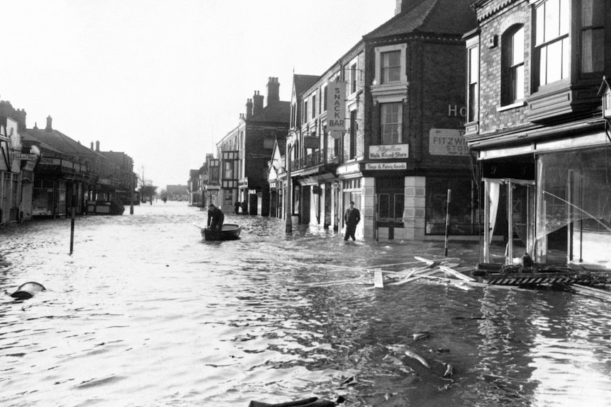 A man in a dinghy on a flooded street that looks like a river flanked by buildings