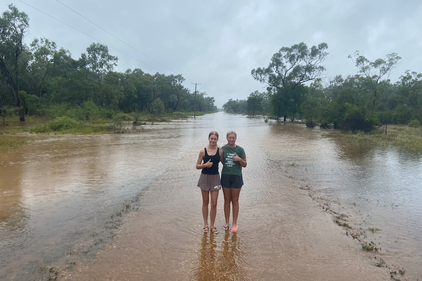 Two teeenage girls standing in shallow flood water. 