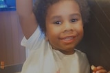 A smiling toddler with a mass of curly hair.