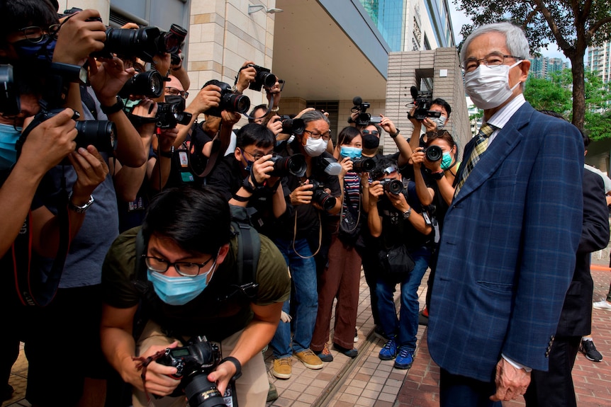 Martin Lee stands in a suit in front of a large group pf men holding cameras