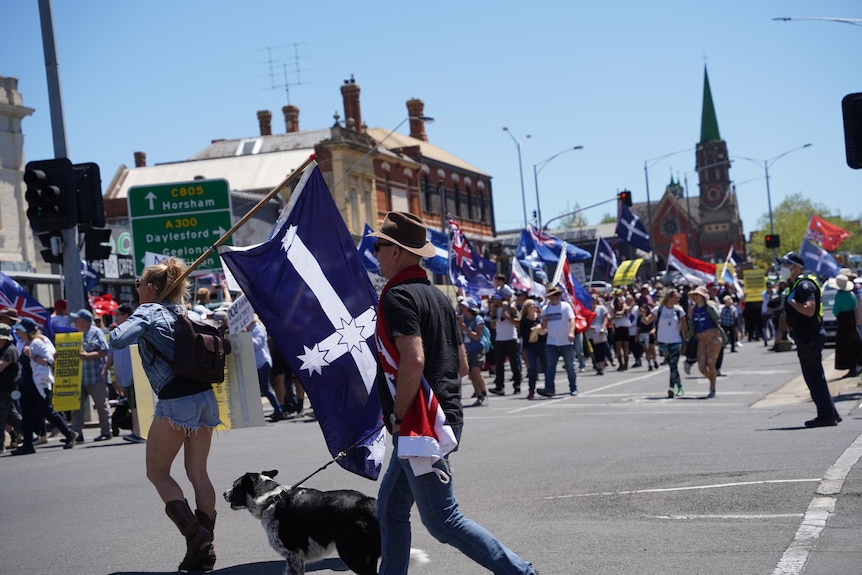 Protesters, many holding Eureka flags, walk through a Ballarat street.