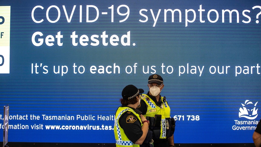 Two police officers under a sign about COVID-19 tests