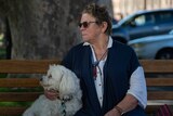 A lady sits with her dog on a park bench.