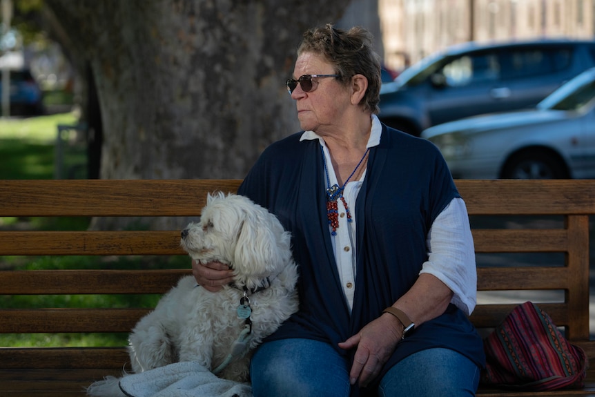 A lady sits with her dog on a park bench.
