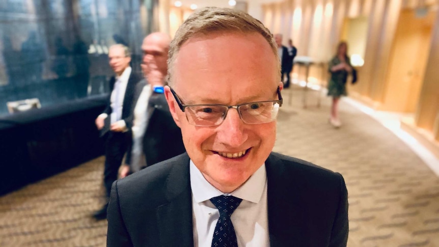 RBA governor Philip Lowe smiles while standing in a hotel lobby after delivering a speech.