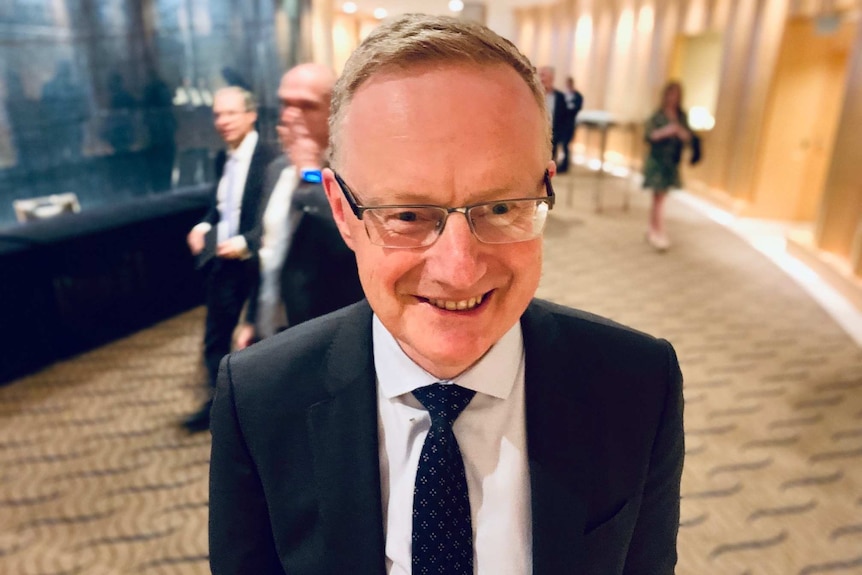 RBA governor Philip Lowe smiles while standing in a hotel lobby after delivering a speech.