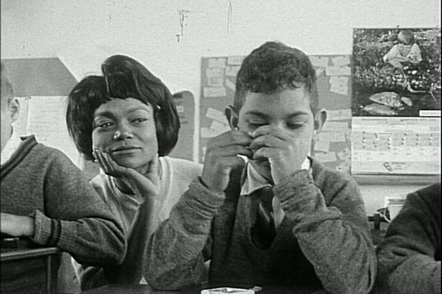 Eartha Kitt sits smiling at boy who has hands covering face