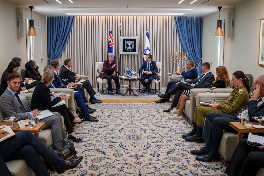 A wide shot of a meeting room in which Australian and Israeli representatives sit on opposite sides. Flags of both countries
