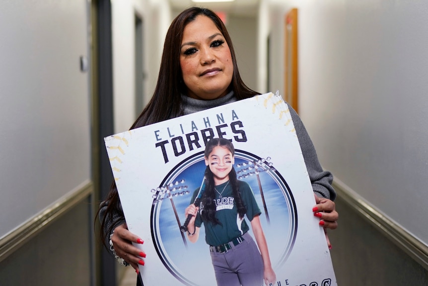 A woman holds a large poster showing a young girl in baseball gear.