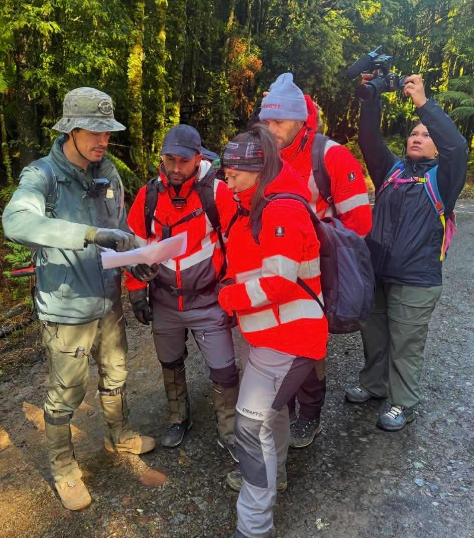 Un grupo de cinco personas con equipo de alta visibilidad mira un mapa y lo señala.