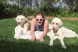 A woman laying on grass with dogs on either side of her.