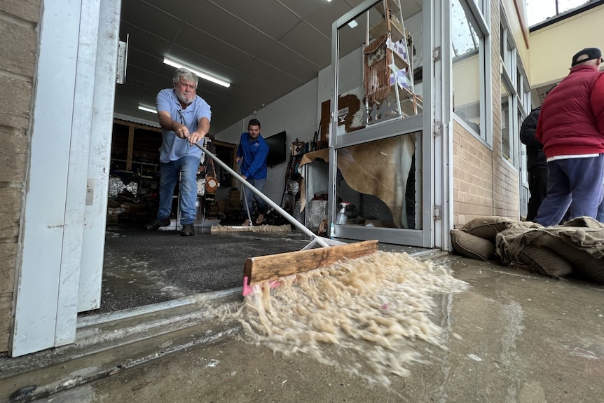 A man uses a large broom to move water out of his flooded business.