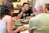 a man eating and smiling at a dinner table with three other people