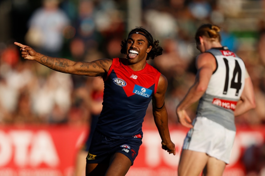 AFL star Kysaiah Pickett smiles and points towards the crowd as he celebrates a goal during a match.