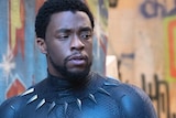 Chadwick Boseman dressed as Black Panther standing in front of a camera.
