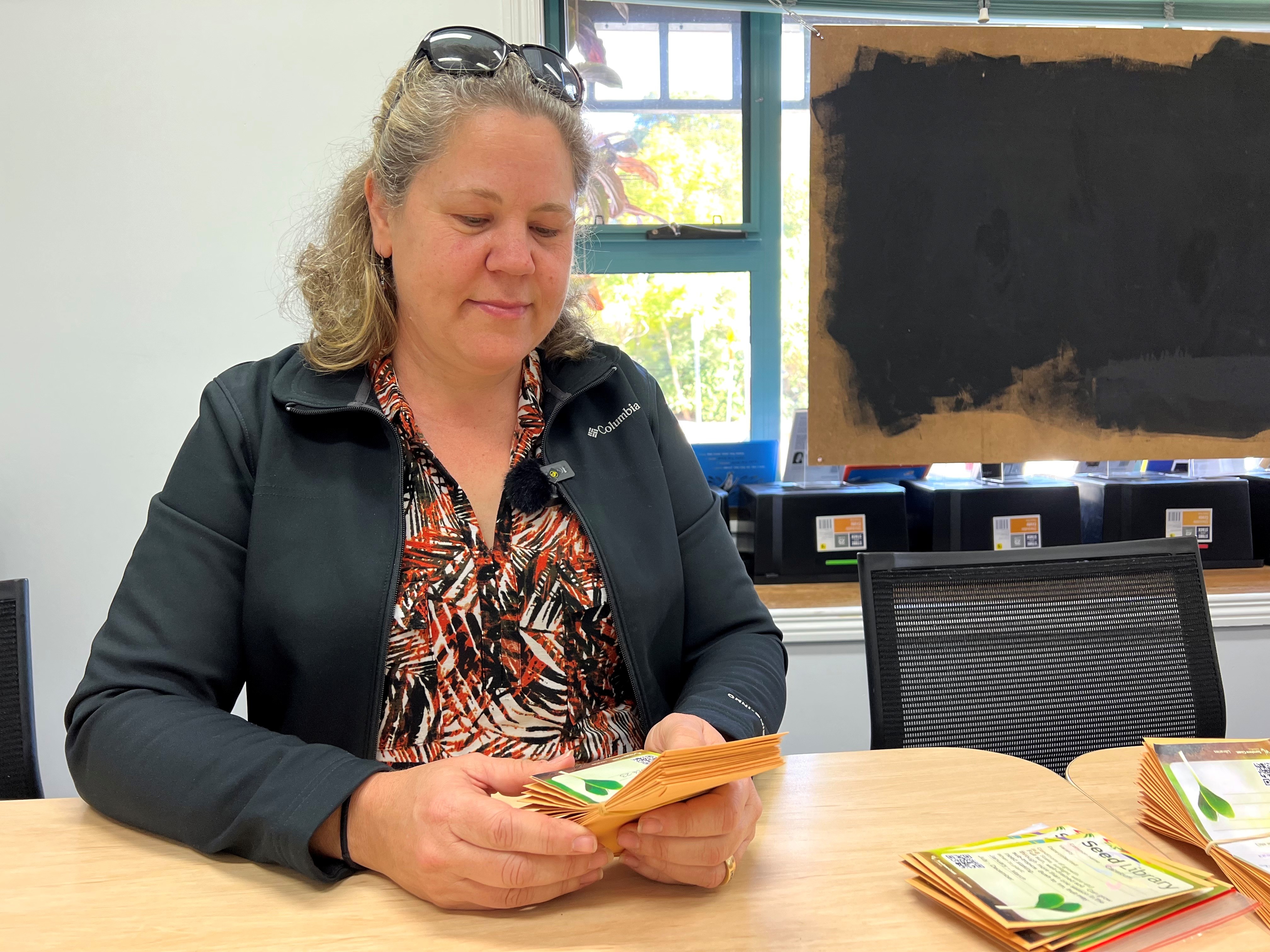 A woman holds packets of seeds in her hands at a table.