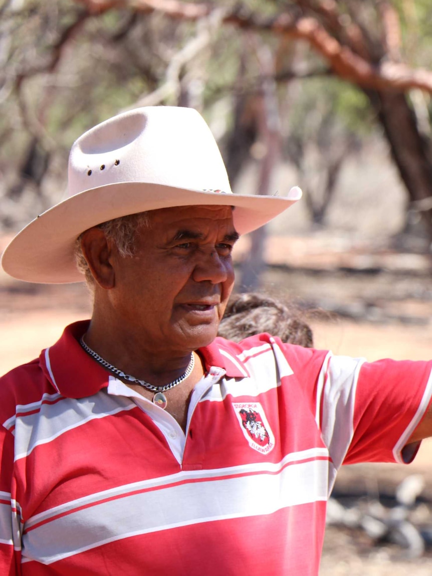 An Aboriginal man standing in the foreground, with out-of-focus trees in the background