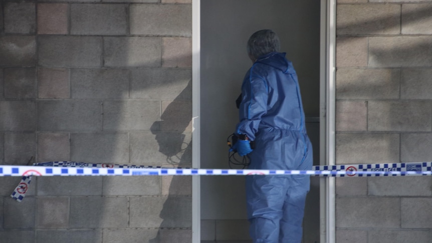 Forensic officer enters a doorway behind a brick wall