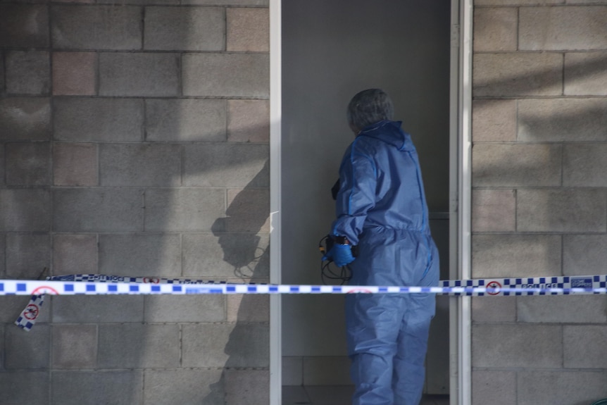 Forensic officer enters a doorway behind a brick wall