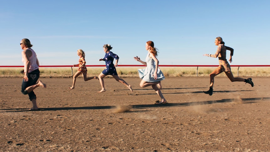 Five women running on a dusty horse racing track.