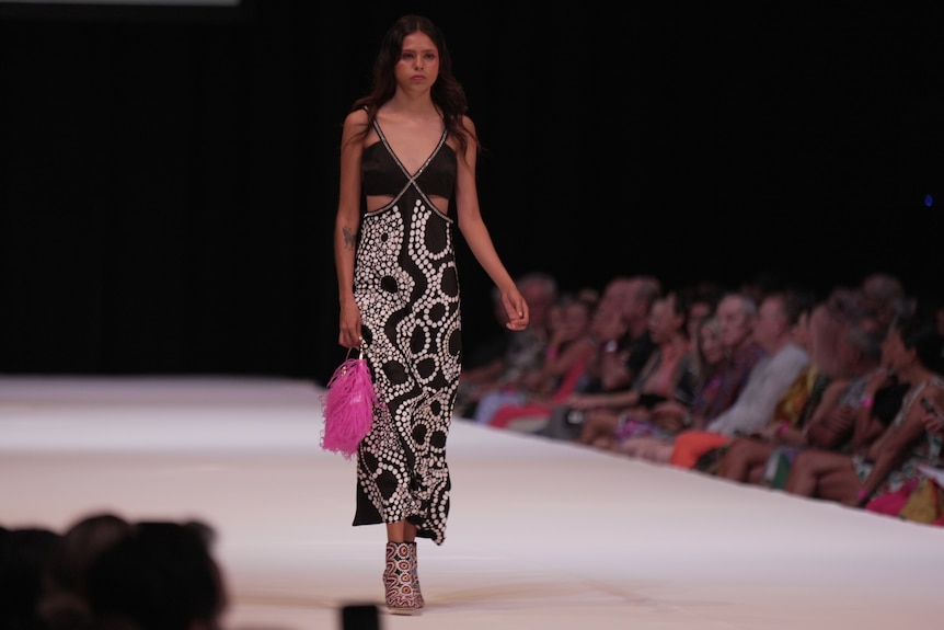 a female model wearing a long patterned dress carrying a hot pink bag