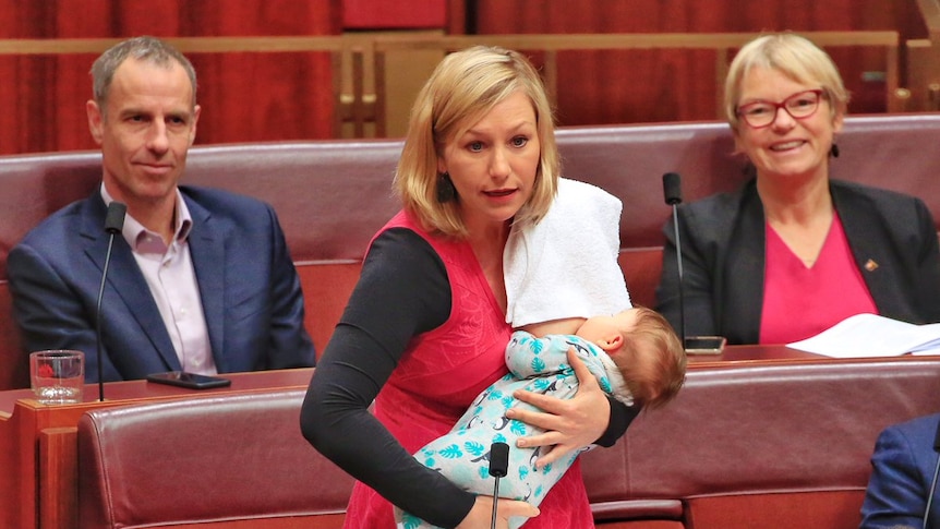 Larissa waters stands in the Senate breastfeeding her baby with a towel slung over her shoulder