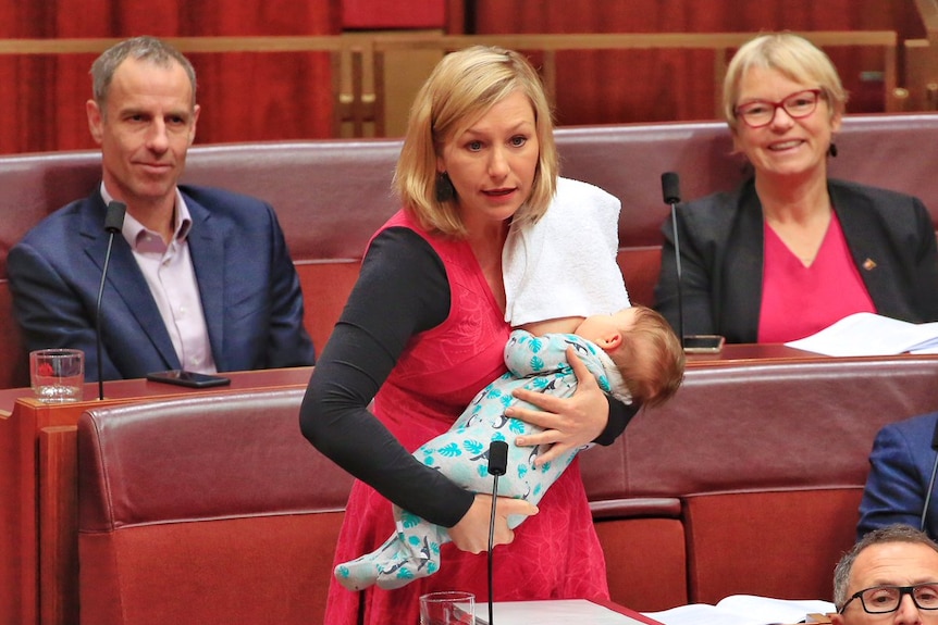 Larissa Waters steht im Senat und stillt ihr Baby mit einem Handtuch über der Schulter