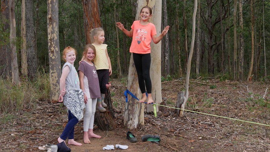 Girl students stand smiling near some gum trees and a tight rope.