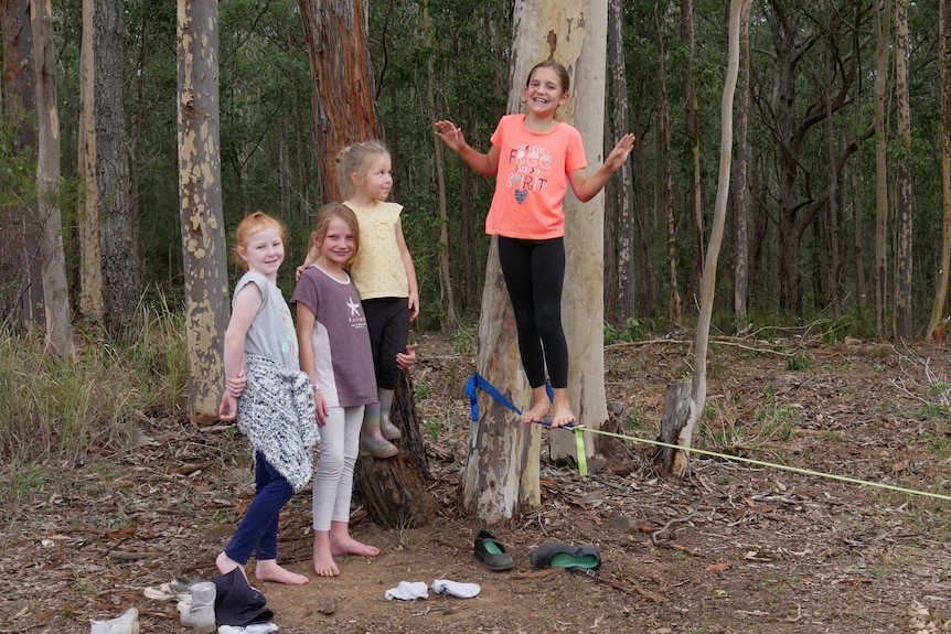 Girl students stand smiling near some gum trees and a tight rope.