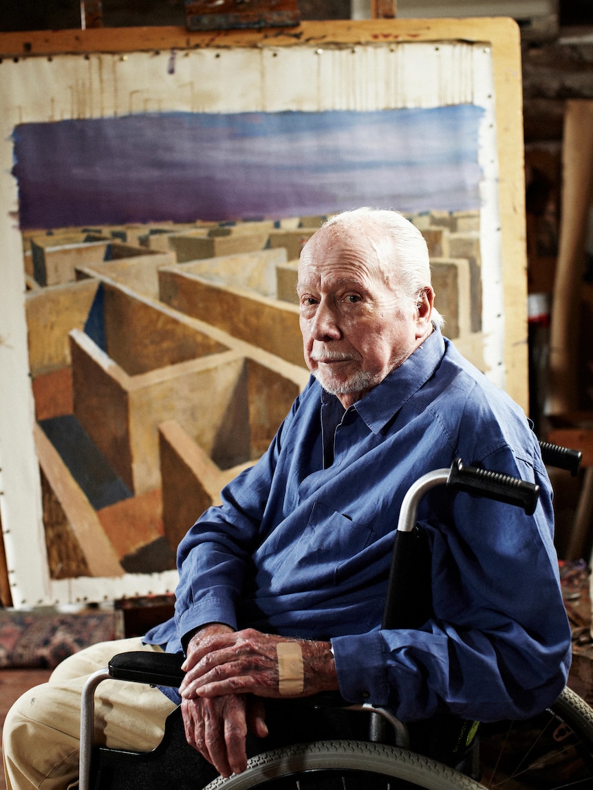 A man in a blue jumper sits is a wheelchair, painting a labyrinth.