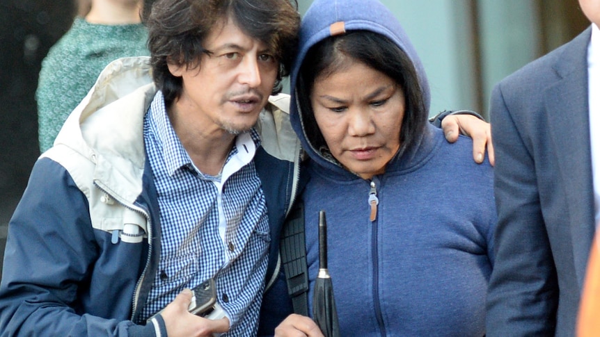 shaggy looking man with his arm around an older woman in a hoodie who is looking down