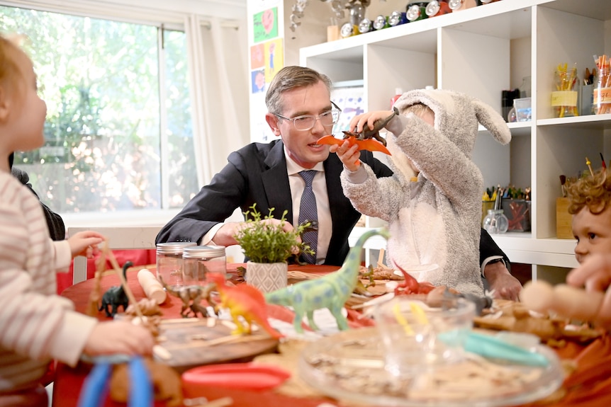 a man wearing glasses talking to a child who is playing with atoy