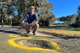 A man squats in front of two big potholes holding a spray can.
