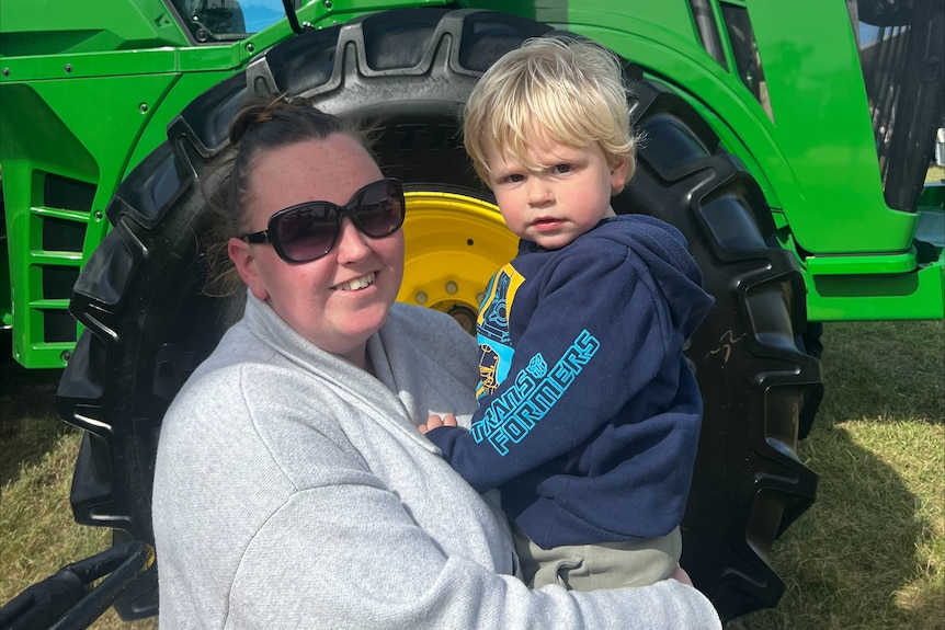 mother holding young son in front of green John Deer tractor 