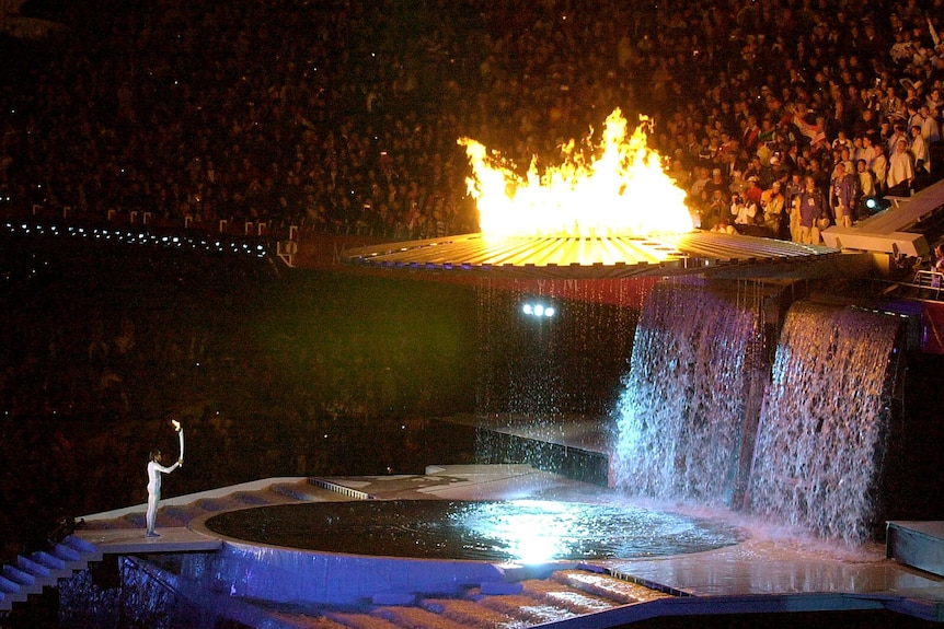 Cathy Freeman holds up an lit torch as a flaming olympic cauldron begins to rise up the stadium side.