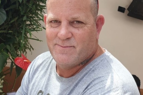 Close up of Will Barabas smiling, wearing a grey t-shirt with plants in the background.