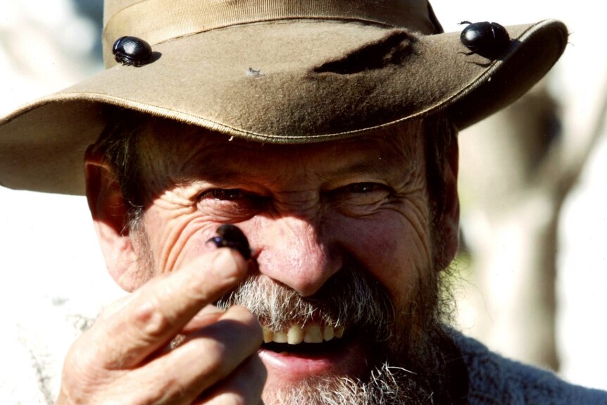 A close-up of a man's smiling face as he hold out a dung beetle.
