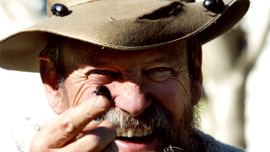 A close-up of a man's smiling face as he hold out a dung beetle.