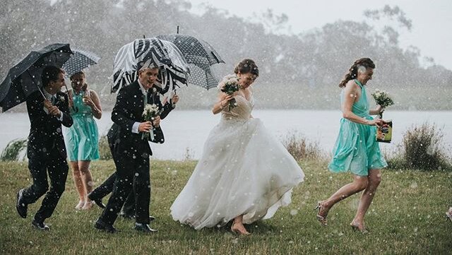 A bridal covers tries to seek cover under umbrellas in pouring