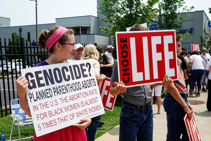 Protesters hold signs.