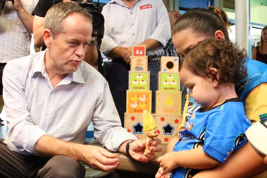 Bill Shorten gives a toy troll to a toddler.