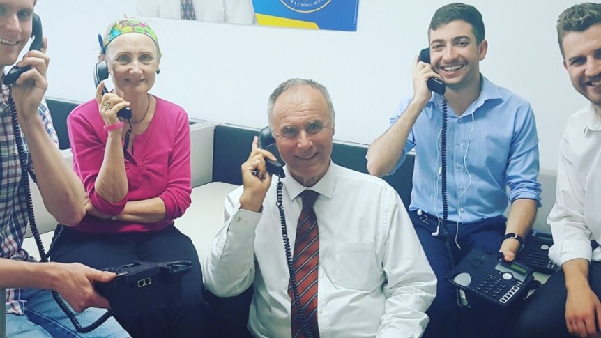 Five people look at the camera, holding phones to their ears.