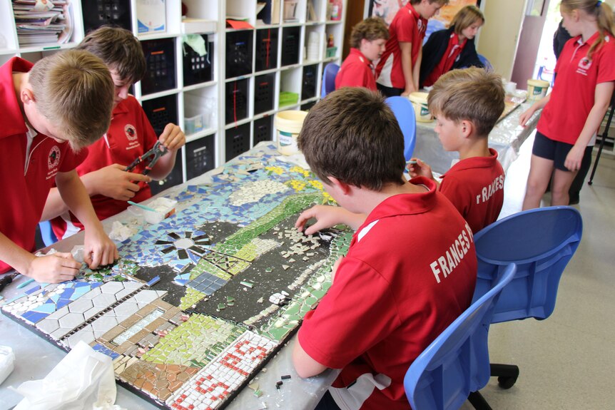 A group of students in red uniforms gathered around a mosaic