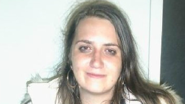 A young woman with long brown hair poses for a photo with her arms crossed.