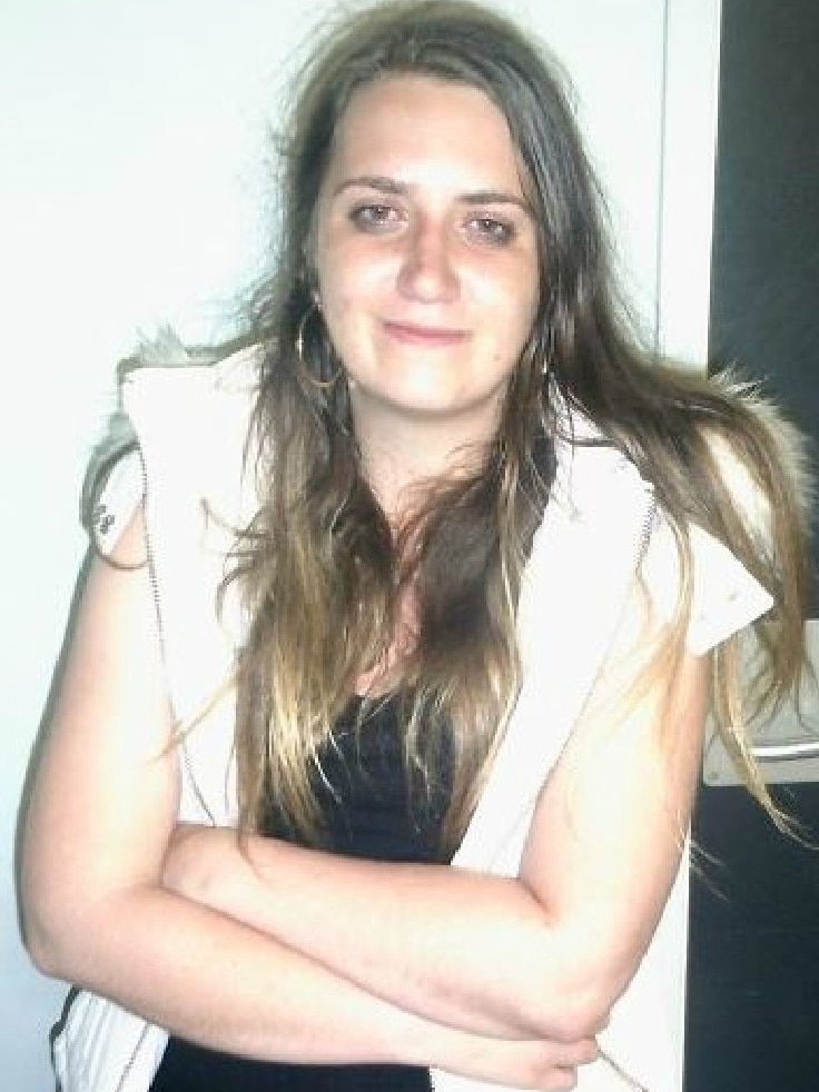 A young woman with long brown hair poses for a photo with her arms crossed.