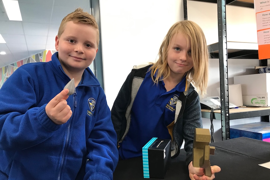 Two boys looking at camera holding 3d printed products.