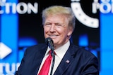 Former US President Donald Trump smiles while delivering a speech