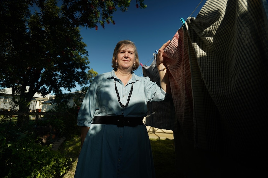 A woman stands with laundry on a hills hoist.