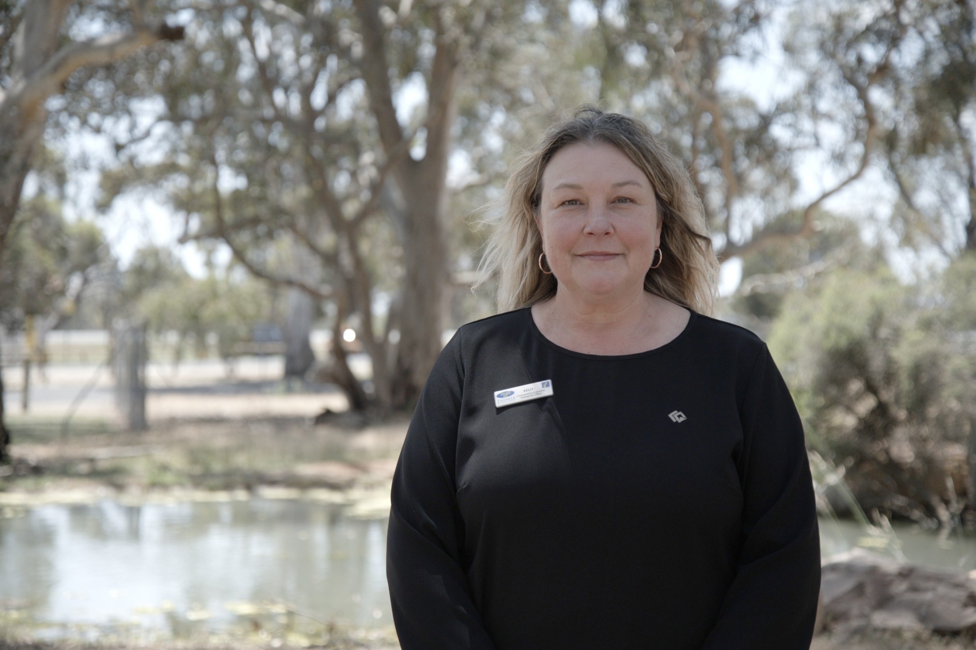 Una mujer con cabello rubio y un top negro se encuentra en un parque de vida silvestre.