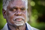 An elderly Indigenous man wearing a suit looks at the camera